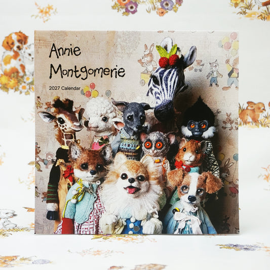 A calendar cover featuring a group of whimsical, plush animal figures, including a zebra, giraffe, fox, and dog, all dressed in colourful clothing. The text reads "Annie Montgomerie 2027 Calendar" against a patterned background.