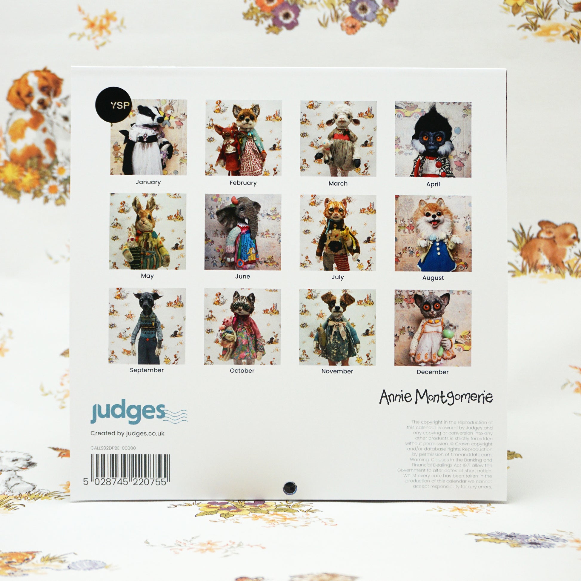 Back cover of a calendar featuring twelve images of whimsical animal figurines dressed in vintage clothing, each representing a month. The background has a floral pattern. The bottom includes branding and a barcode.