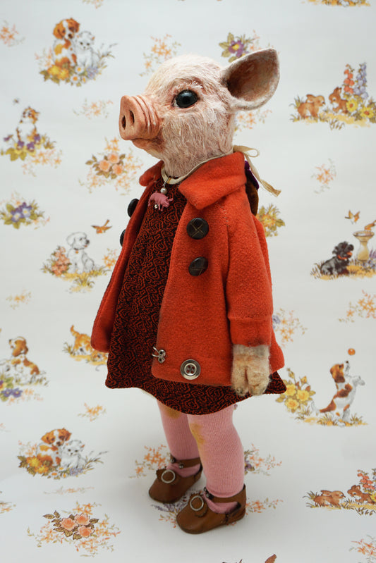 A pig with a pink snout and ears, wearing a bright orange coat over a dark patterned dress, pink tights, and brown shoes, standing against a white patterned backdrop with dog illustrations.