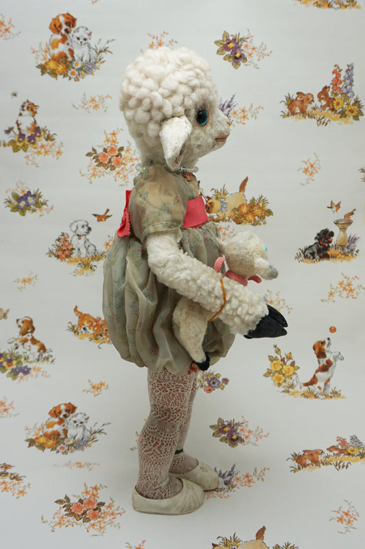 A plush lamb toy dressed in a floral dress with a red sash, holding a smaller lamb toy. The background features a whimsical pattern of animals and flowers, including dogs and rabbits, in soft pastel colours.