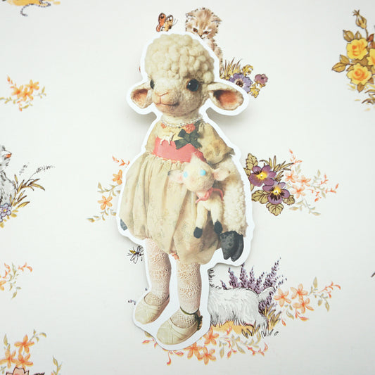 A shaped postcard of a plush lamb dressed in vintage-style clothing, holding a smaller lamb toy. The background features a floral pattern with butterflies and a small dog, creating a whimsical and nostalgic atmosphere.