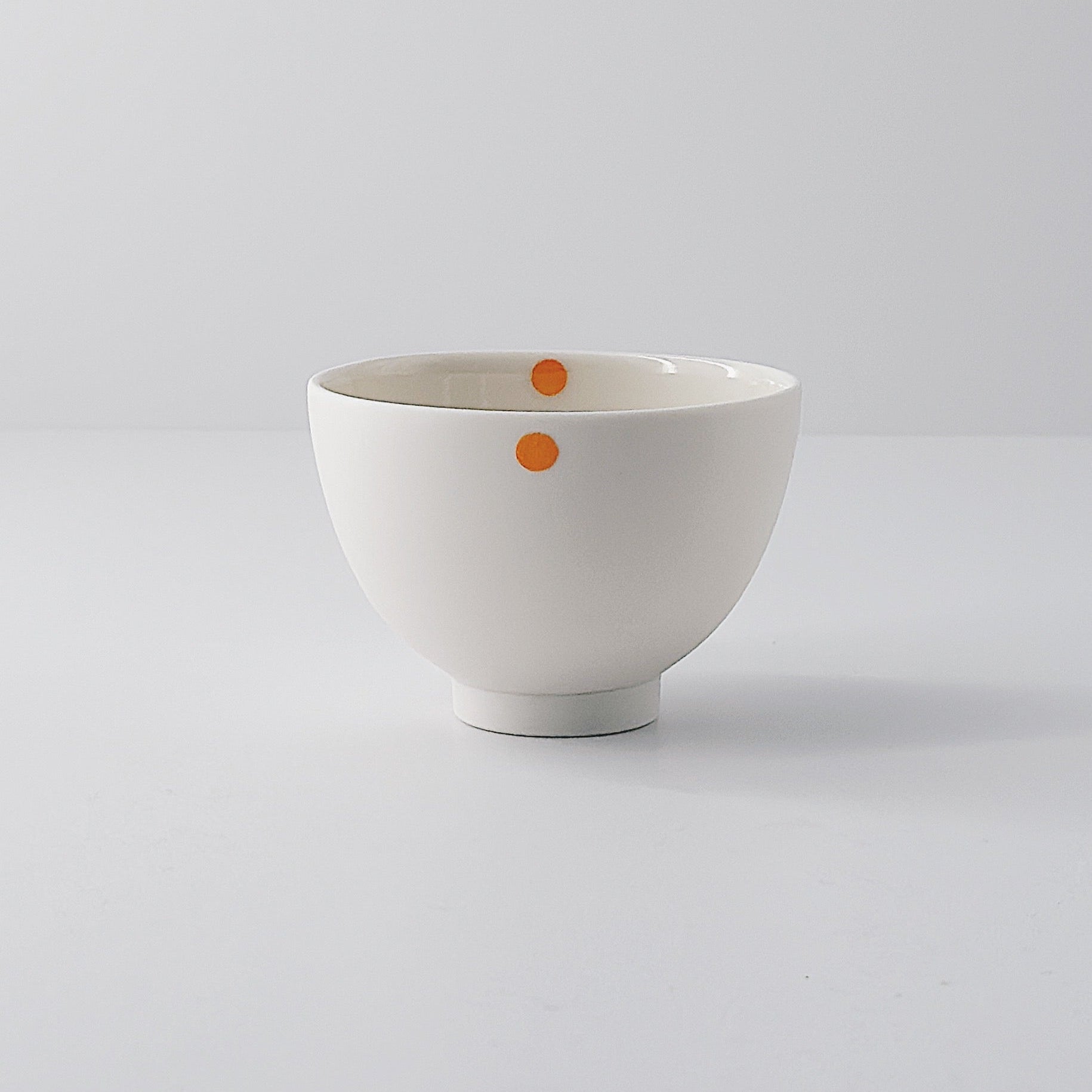 White porcelain bowl with a single orange dot on a light grey background