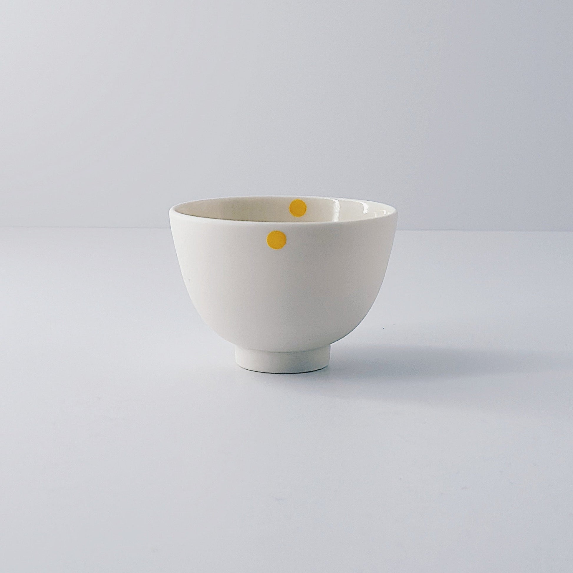 White porcelain bowl with a single yellow dot on a light grey background