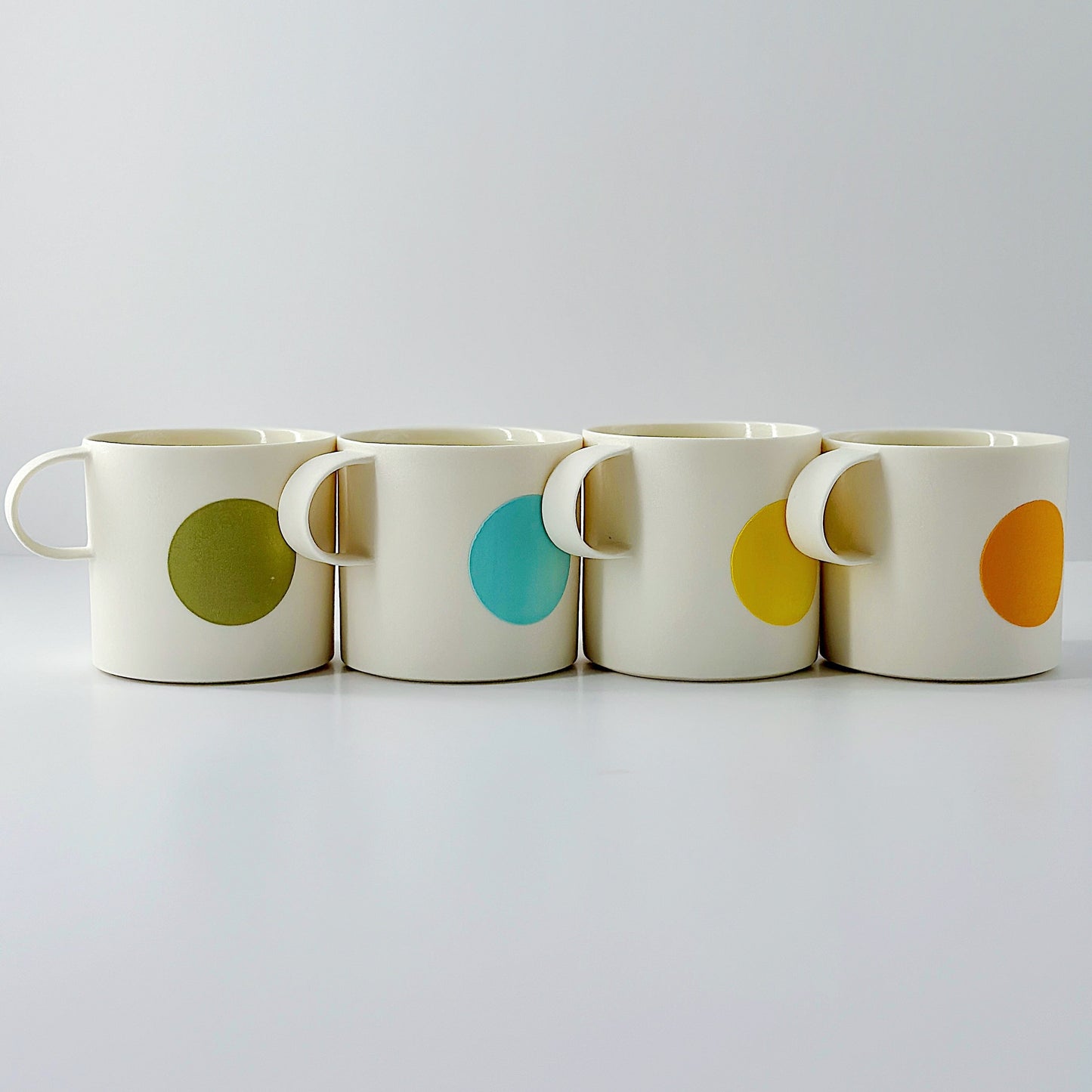 Four ceramic mugs with colorful circular patterns on a white background