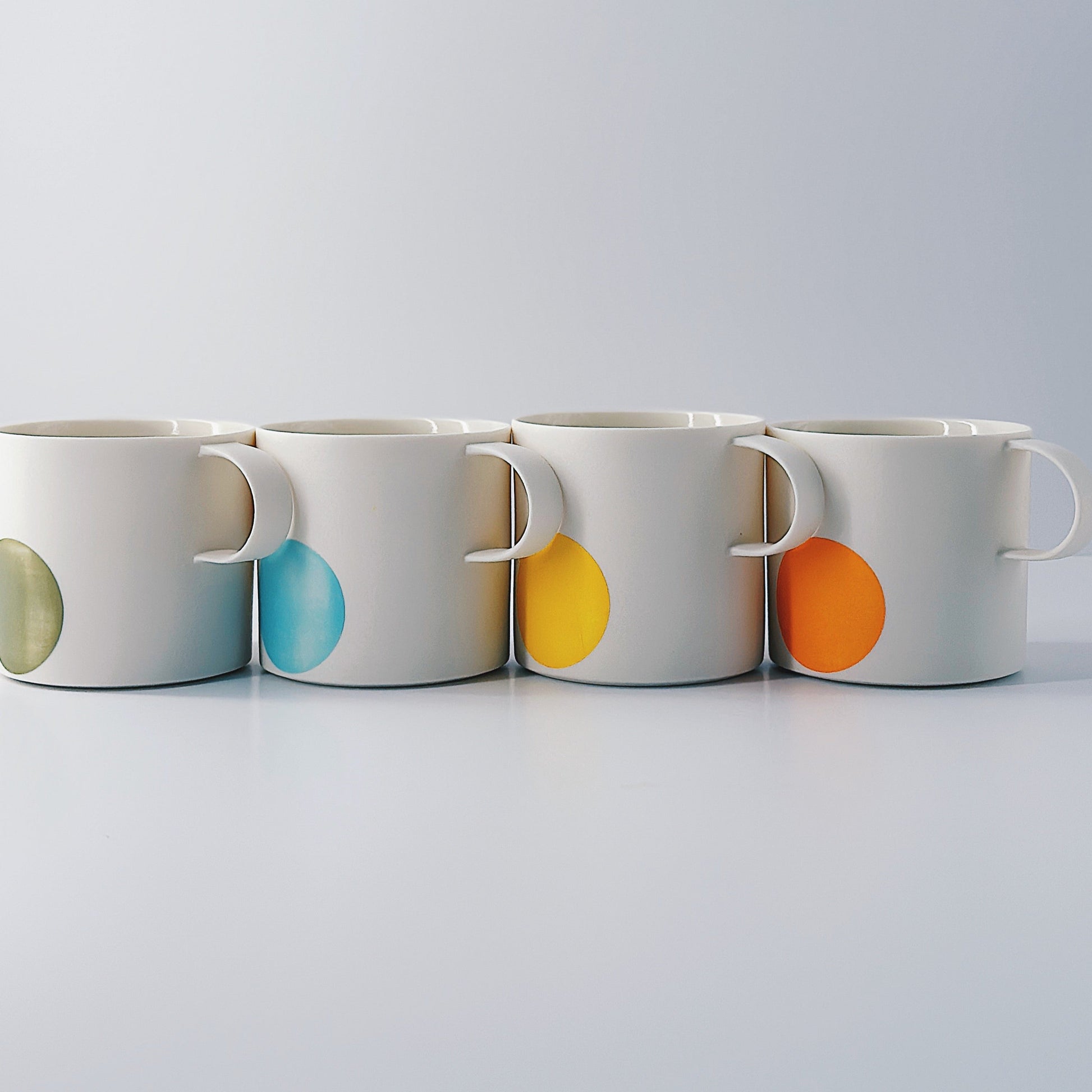 Four white mugs with colourful dots on a light grey background
