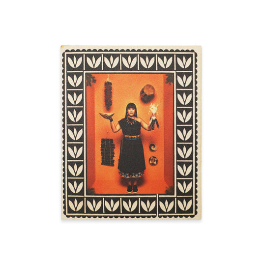 A woman stands against an orange background, holding a bird and a doll. She wears a black dress with decorative trim. The image is framed with a black and white leaf pattern. Various objects hang on the wall, including a hat and a crescent moon.