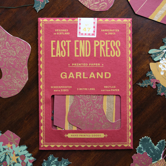Pink packaging of East End Press Garland on a wooden surface with decorative paper pieces.