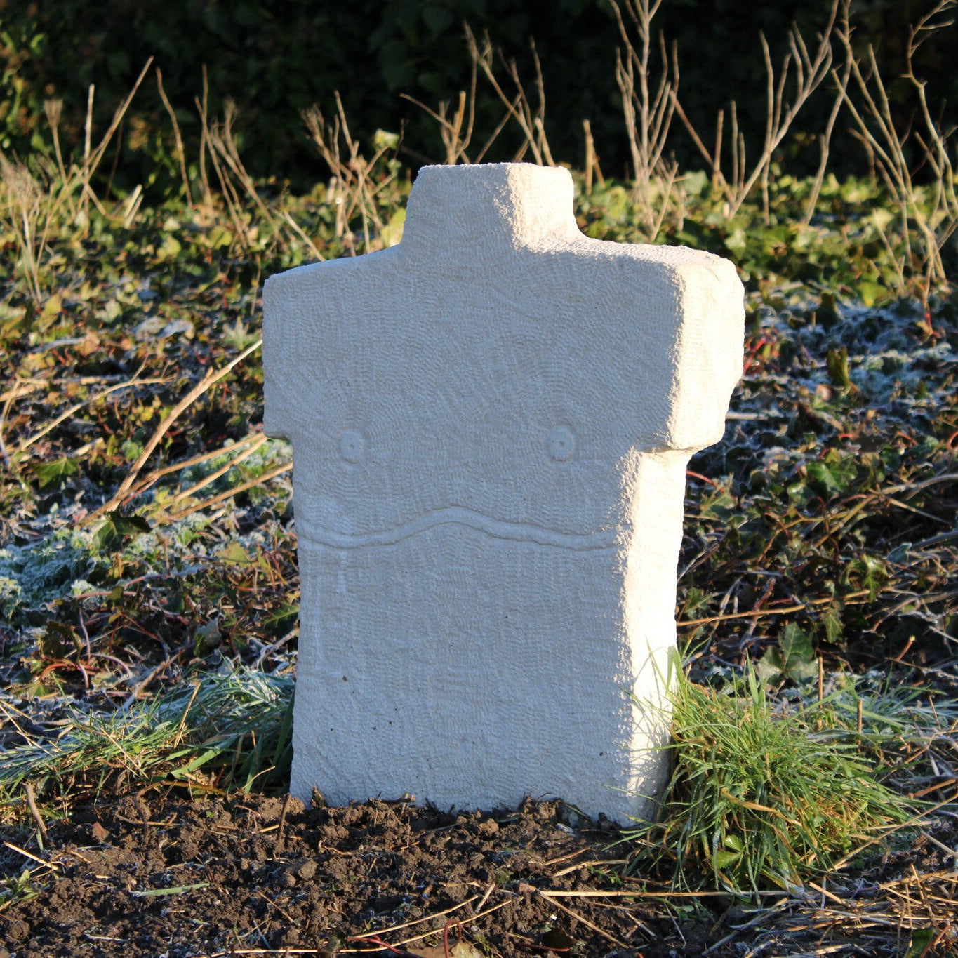 White headstone  on a grassy field with a blurred background. The headstone resembles a torso with surgery scars.
