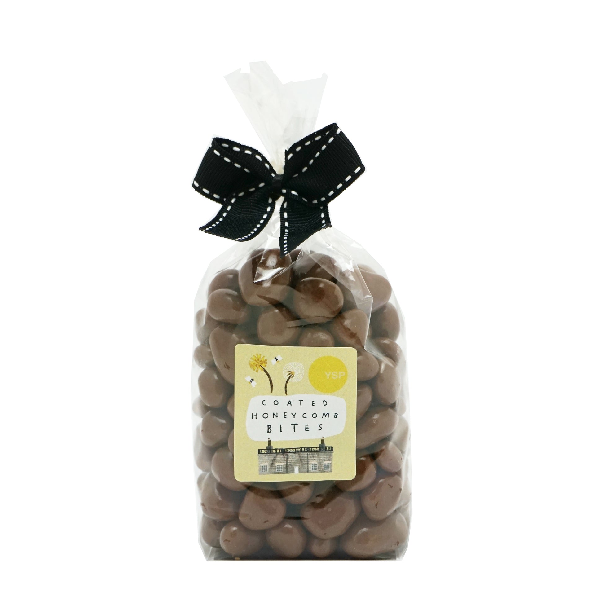 A clear bag of milk chocolate coated honeycomb bites, tied with a black ribbon. The label is yellow and features an illustration of a building and some flowers.
