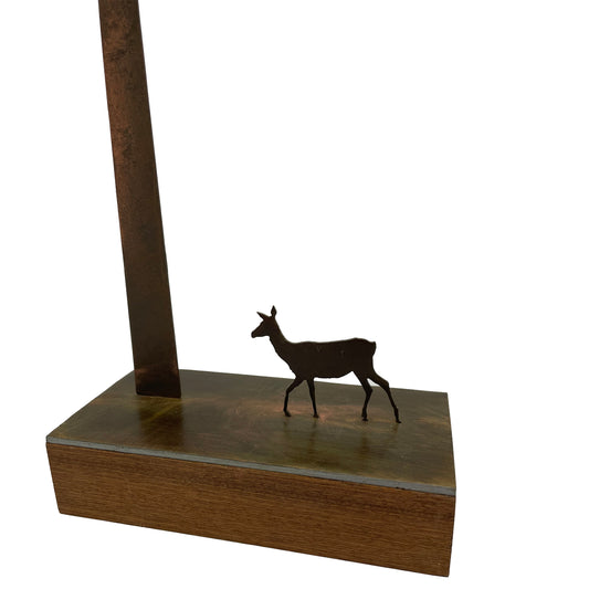A close up detail of a single laser cut metal deer standing under a very tall single tree.