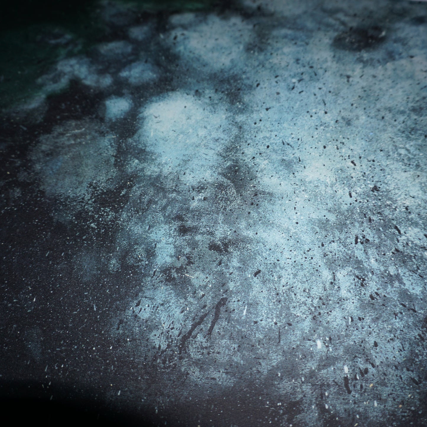 Abstract image featuring a textured surface with a mix of dark and light blue tones, resembling a cosmic or underwater scene. The pattern includes speckles and patches, creating a sense of depth and movement across the composition.