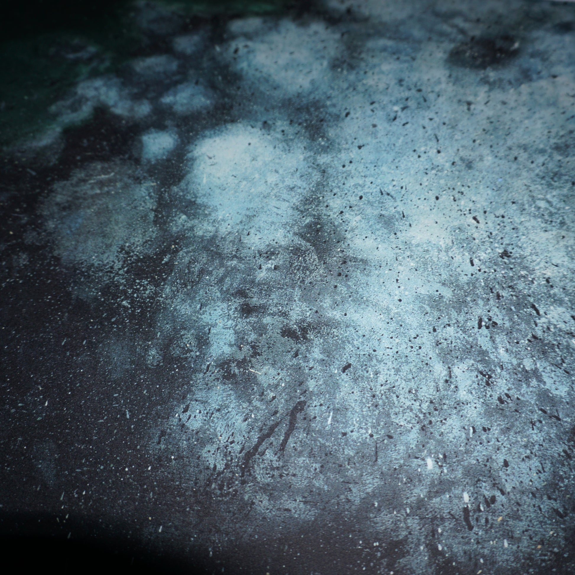 Abstract image featuring a textured surface with a mix of dark and light blue tones, resembling a cosmic or underwater scene. The pattern includes speckles and patches, creating a sense of depth and movement across the composition.