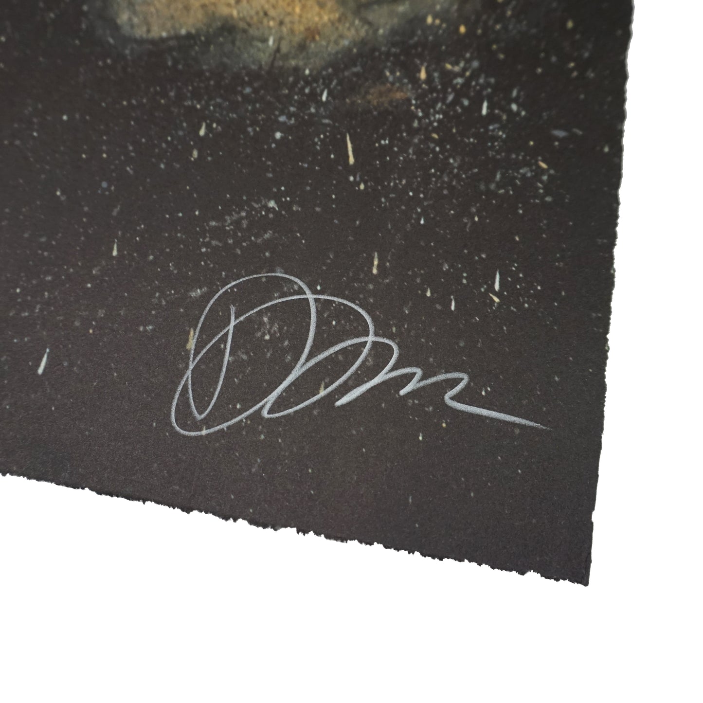 Close-up of a dark, textured surface with a white signature in the bottom corner. The background features scattered specks resembling stars or dust, creating a cosmic effect. The signature is stylised and prominent against the dark backdrop.