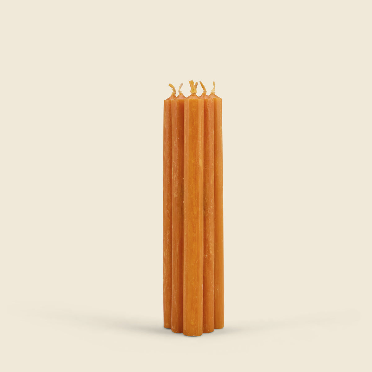 A set of five orange taper candles standing upright and slightly fanned out, photographed against a solid, warm off-white background.