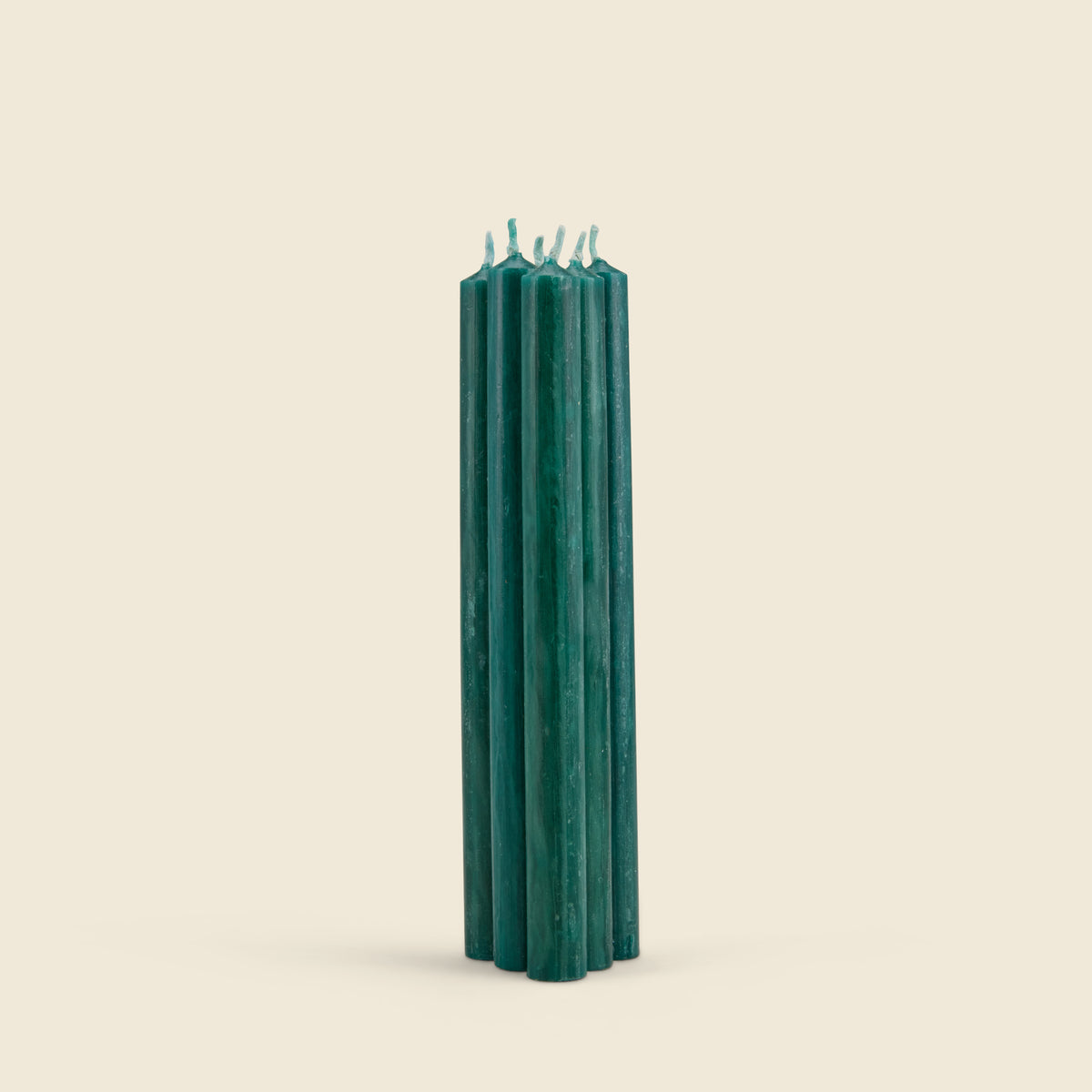 A cluster of tall, dark teal green pillar candles standing upright against a solid, warm off-white background.
