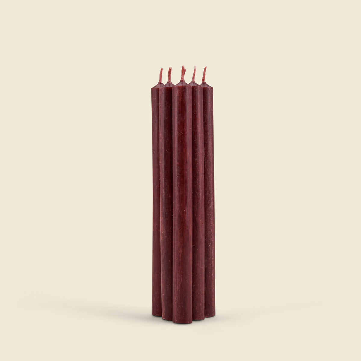 A set of five dark burgundy taper candles standing upright and slightly fanned out, photographed against a solid, warm off-white background.
