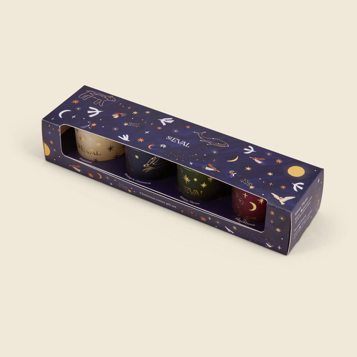 A boxed set of four candles in a dark navy starry-night themed box with a clear window showing the candles inside. The candles are cream, dark blue, green, and burgundy, each with gold celestial illustrations.