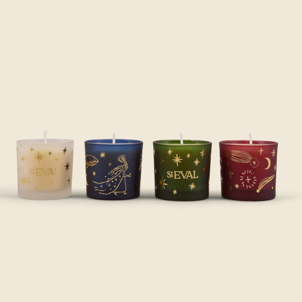 Four decorative glass candle holders with wicks, each featuring a different celestial design and the name 'ST EVAL' in gold lettering. The candles are in cream, navy blue, dark green, and burgundy, set against a solid light beige background.