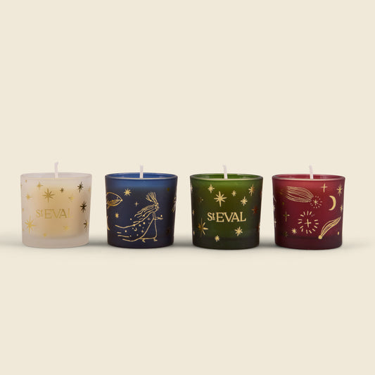 Four decorative glass candle holders with wicks, each featuring a different celestial design and the name 'ST EVAL' in gold lettering. The candles are in cream, navy blue, dark green, and burgundy, set against a solid light beige background.