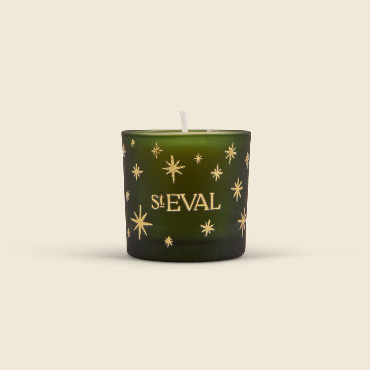 A dark green glass candle with gold starburst patterns and the text 'St Eval' printed on the front, set against a solid light beige background.