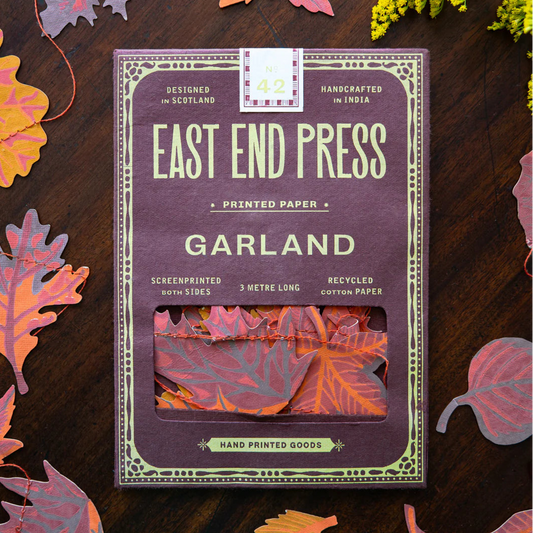 East End Press Garland packaging with decorative cut-out leaves in shades of orange and brown on a wooden surface