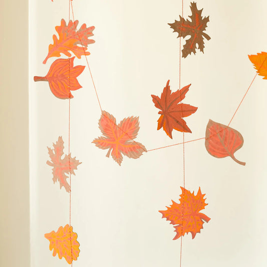 Decorative leaf garland with autumn leaves in shades of orange, red and brown draped against a neutral background.