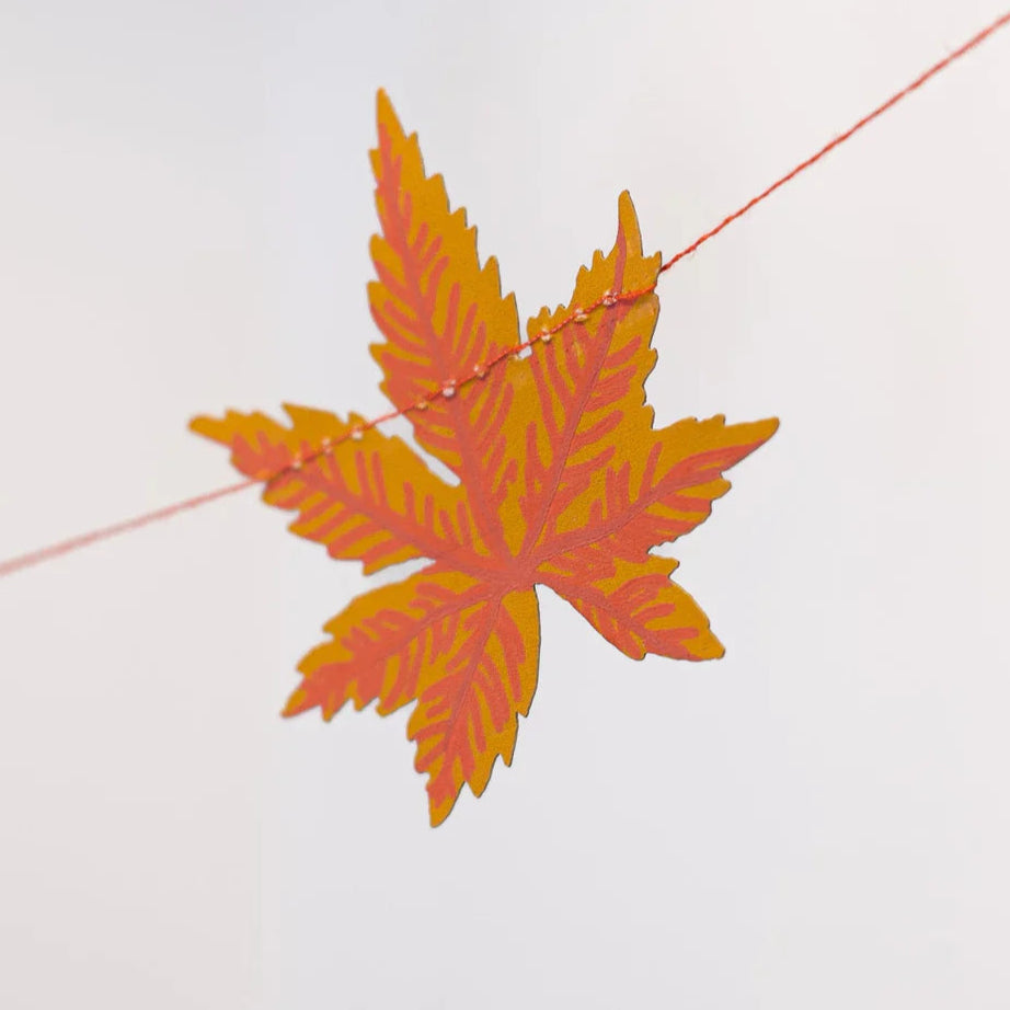Decorative cut out maple leaf in shades of orange and red on a plain white background