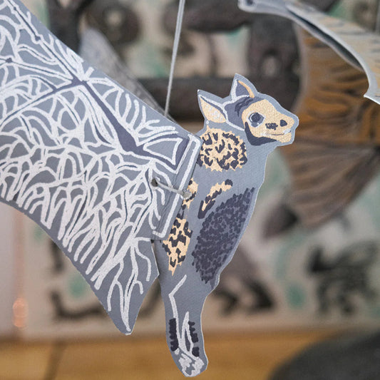 Decorative bat paper cut-out with intricate patterns on a wooden surface. The main colours are grey and beige.