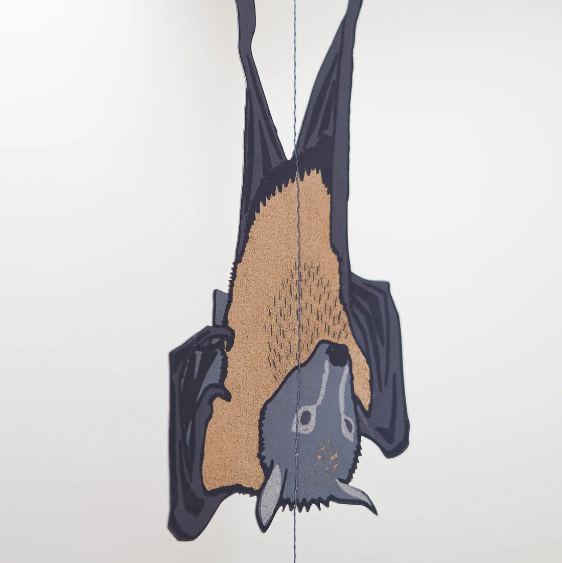 Paper cut out of a bat hanging upside down on a white background. The bat is grey with beige accents.