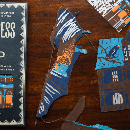 East End Press Garland featuring cut-outs of bats, moons and houses all in shades of blue, brown and orange.