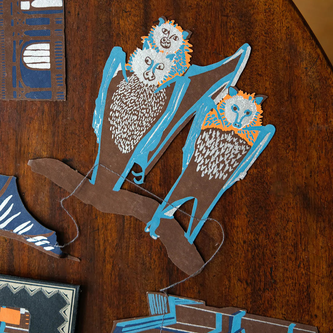 Close up cut-out of three bats hanging upside down from a branch. The main colours are blue, brown and orange.