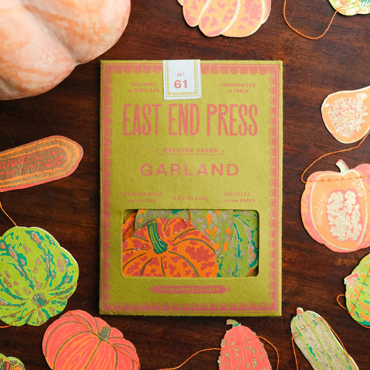 Packaging for a paper sewn garland featuring cut-outs of pumpkins and gourds on a wooden surface. The main colours are orange and green.