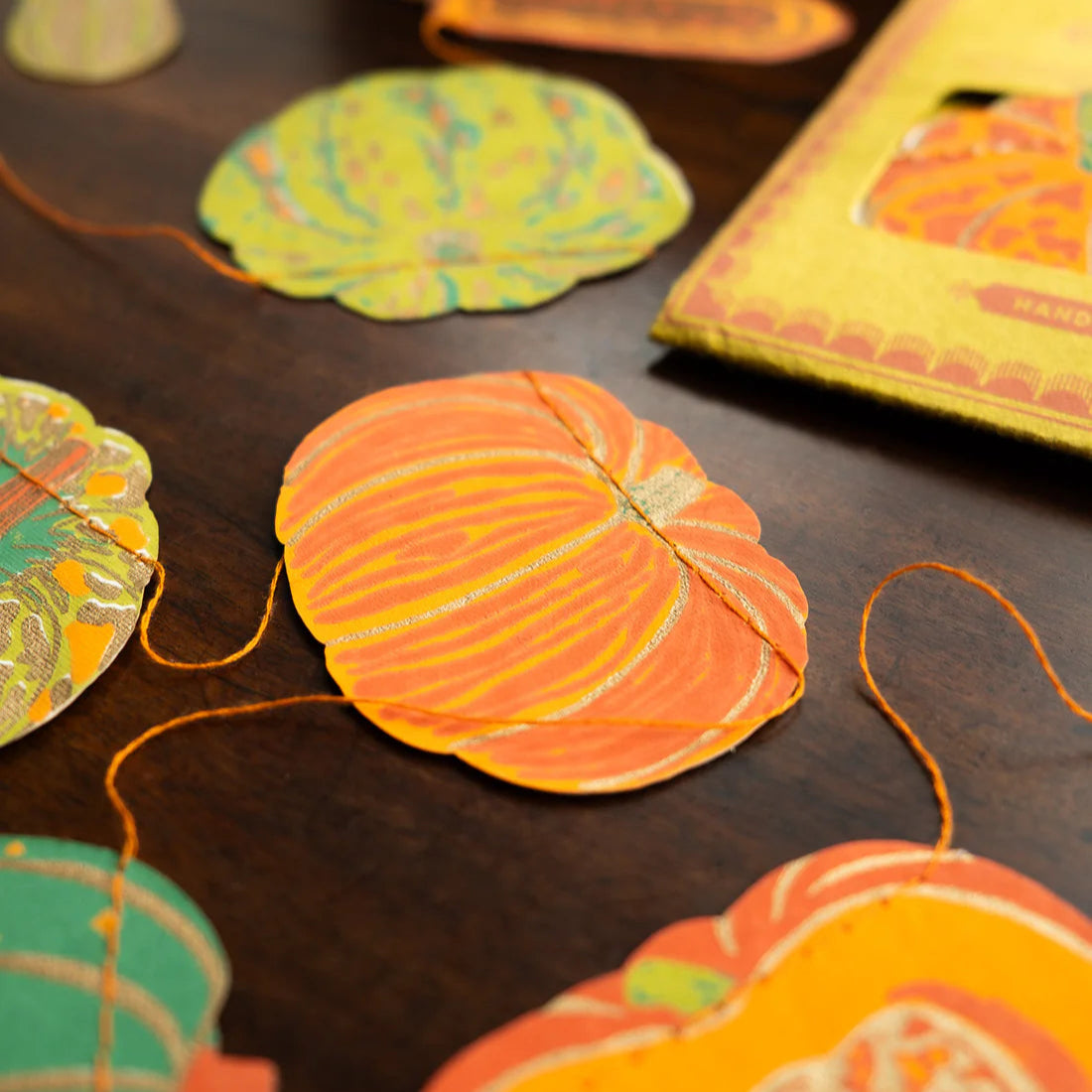 Decorative paper pumpkins in shades of orange and green on a dark surface with a box in the background