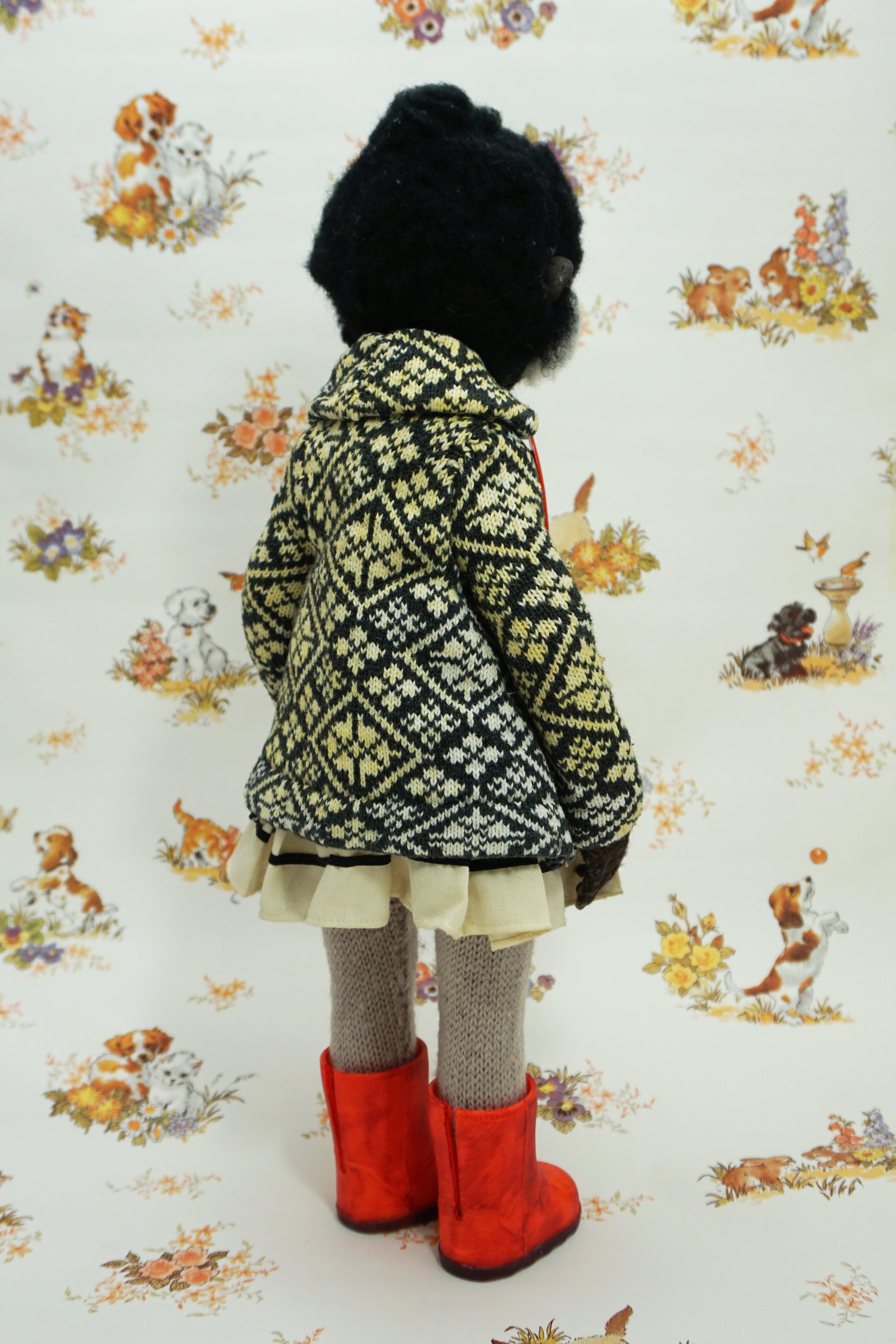 A whimsical doll with a monkey-like face, wearing a patterned coat, white dress, and bright red boots. The background features a vintage-style wallpaper with illustrations of animals and flowers.