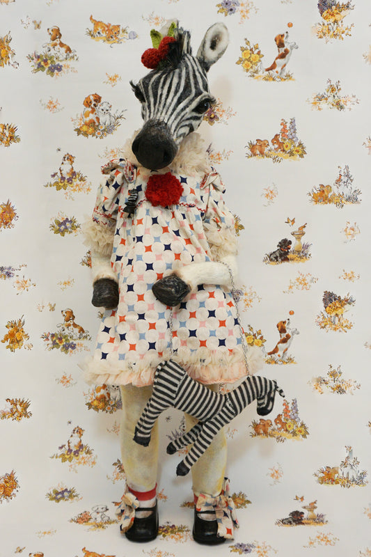 A plush zebra with a patterned dress and red pom-poms stands against a whimsical animal-themed wallpaper. They hold a small zebra toy, and wear black shoes with matching patterned socks.
