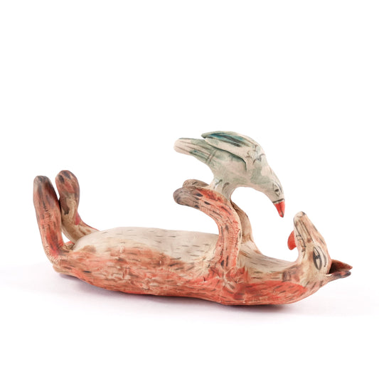A painted ceramic fox whistle in shades of orange and beige. The fox is lying on it's back playing with a bird. Shown on a plain white background.