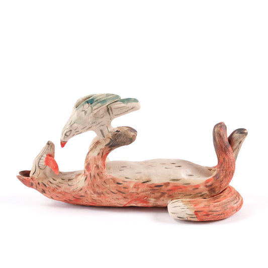 A painted ceramic fox whistle in shades of orange and beige. The fox is lying on it's back playing with a bird. Shown on a plain white background.