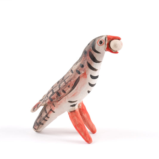 A painted ceramic partridge whistle in shades of brown, beige and orange. The partridge is holding something spherical in its mouth.