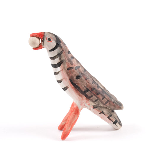 A painted ceramic partridge whistle in shades of brown, beige and orange. The partridge is holding something spherical in its mouth.