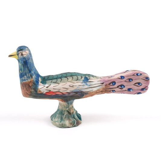 A painted ceramic peacock whistle in shades of blue, pink and green with a yellow beak one a plain white background.