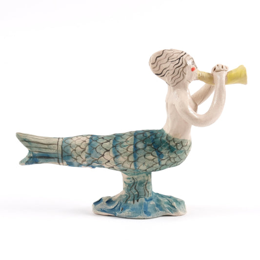 Painted ceramic mermaid whistle blowing a yellow conch shell on a white background, her tail is blue and green.