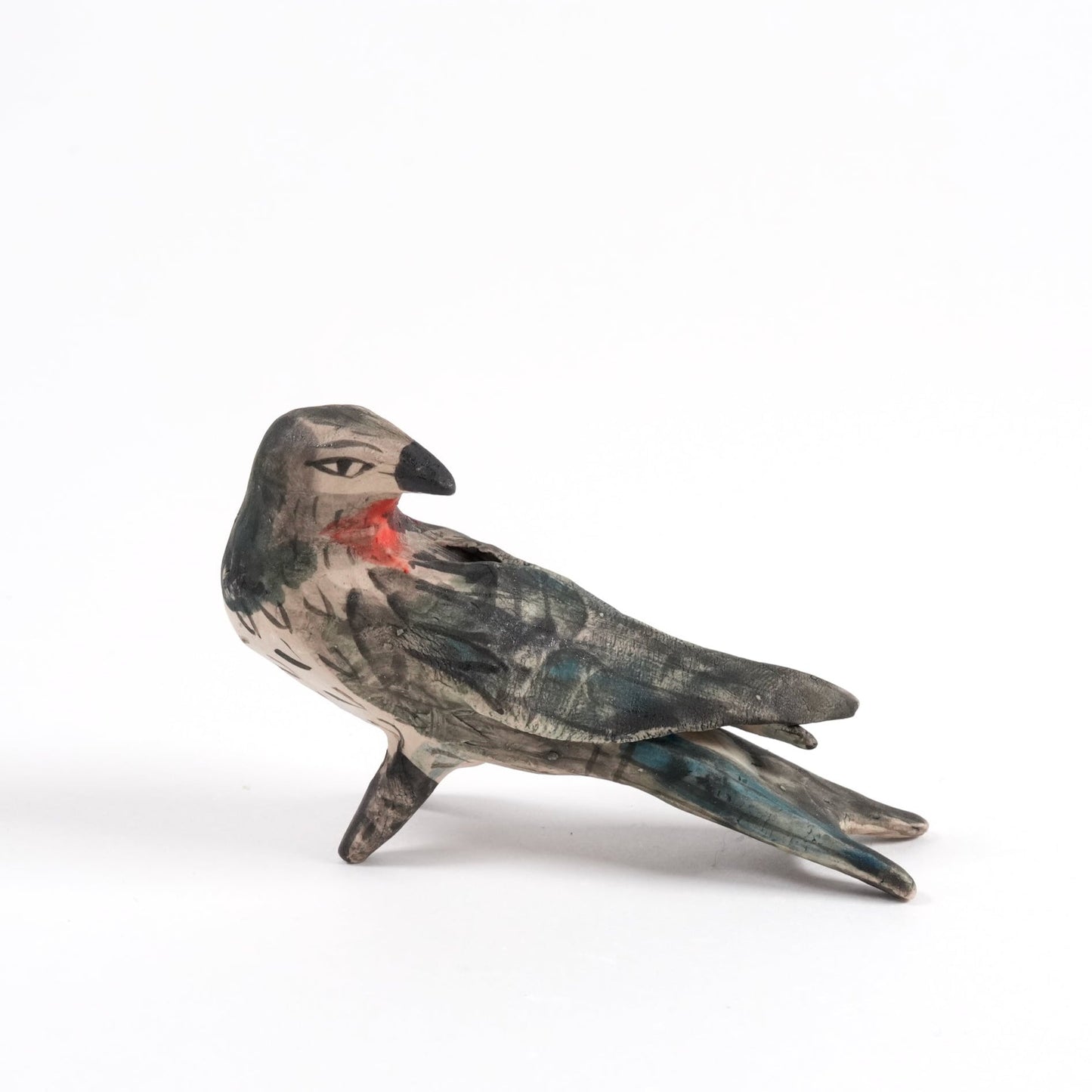A painted ceramic swallow whistle in shades of black and brown standing on a plain white background.