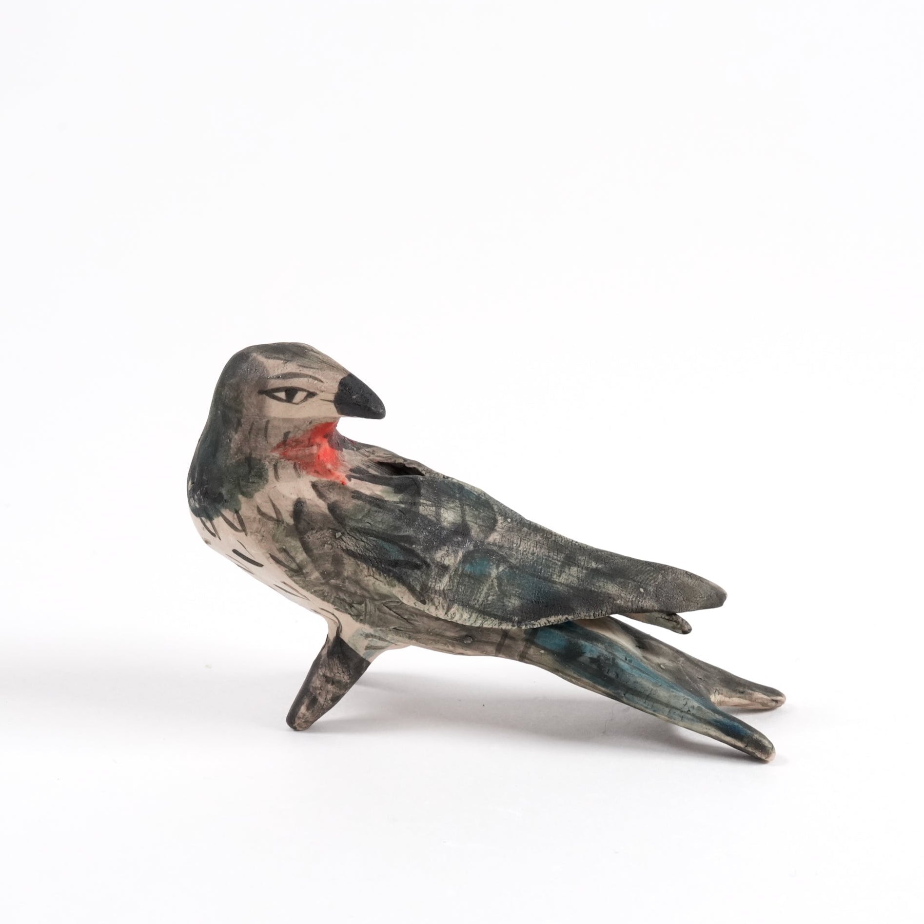 A painted ceramic swallow whistle in shades of black and brown standing on a plain white background.