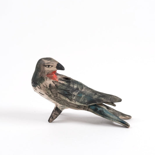 A painted ceramic swallow whistle in shades of black and brown standing on a plain white background.
