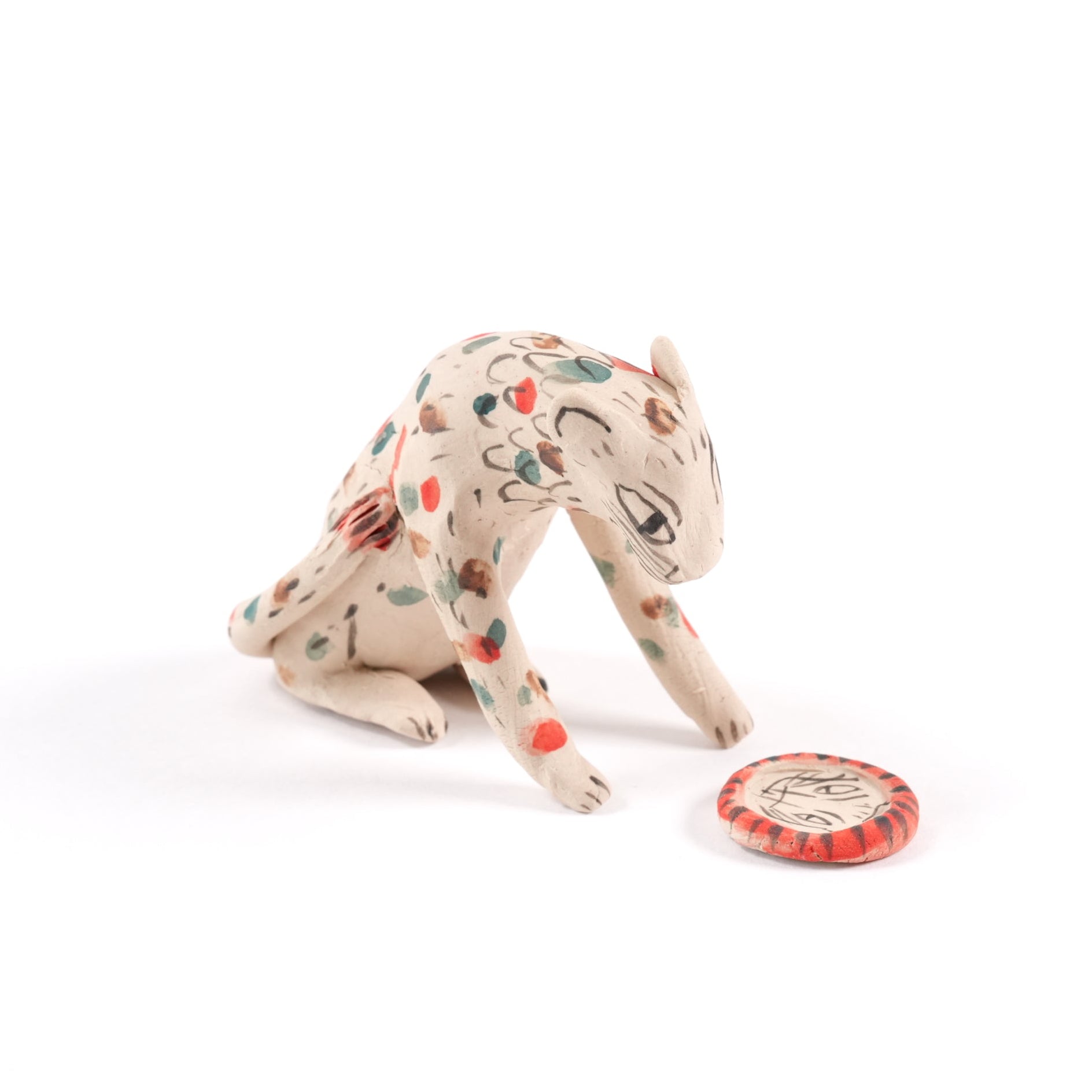 A painted sat ceramic tiger whistle in shades of beige with red, blue and brown spots on a plain white background.