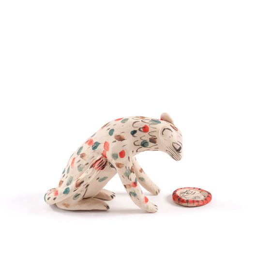 A painted sat ceramic tiger whistle in shades of beige with red, blue and brown spots on a plain white background.