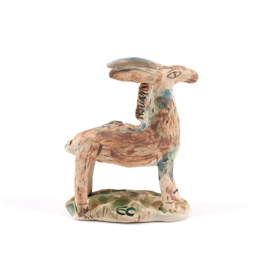 A painted ceramic wild ass whistle in shades of brown and blue standing on a plain white background.