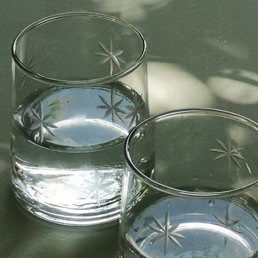 Two clear glass tumblers with starburst patterns on a reflective surface.