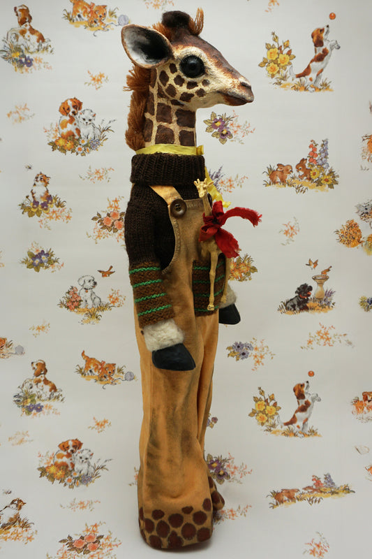A plush giraffe dressed in a brown jumper and trousers, with a smaller giraffe toy attached to its front. The background features a whimsical pattern of animals and flowers in soft colours.