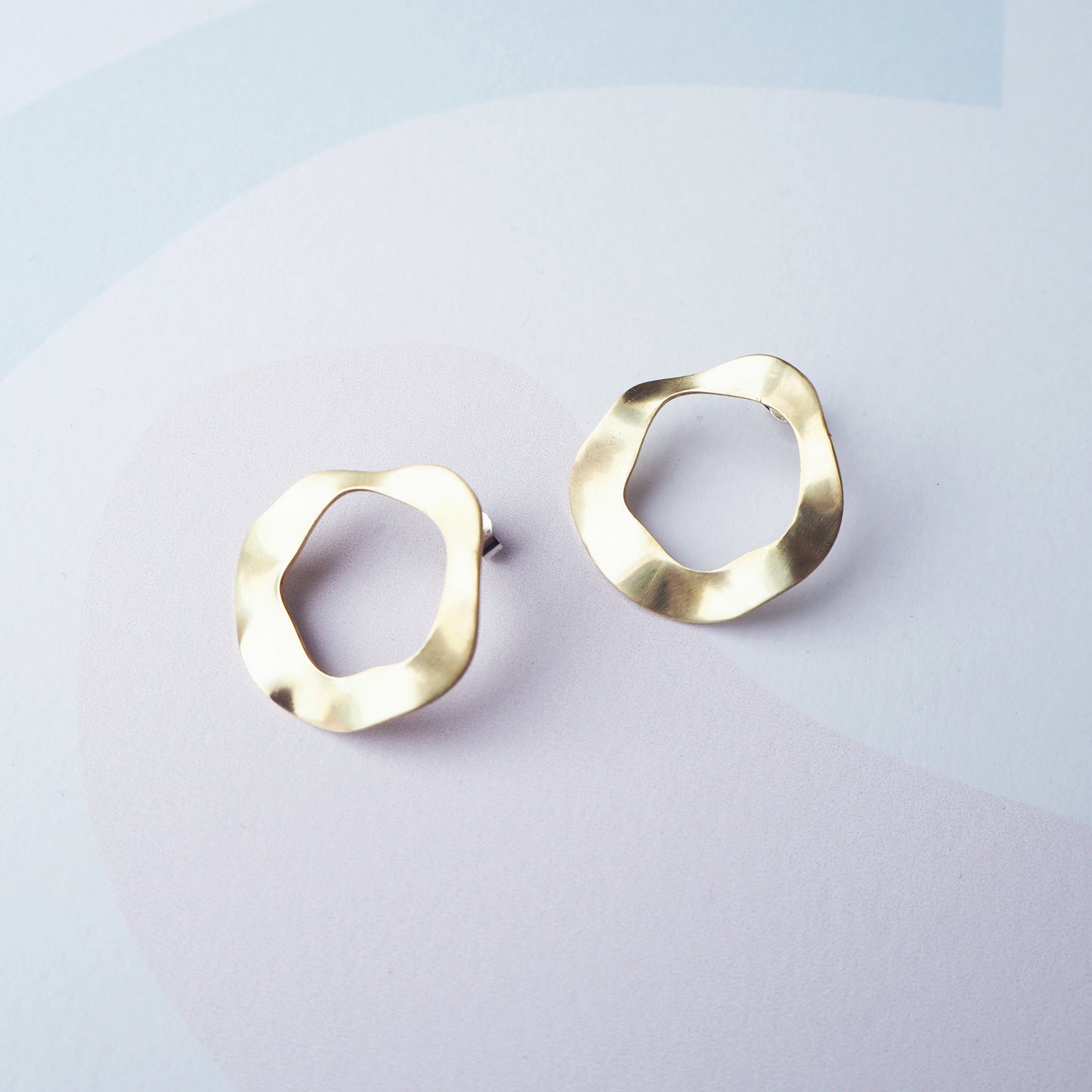 Pair of gold hoop stud earrings with a cut out circular middle on a light grey background